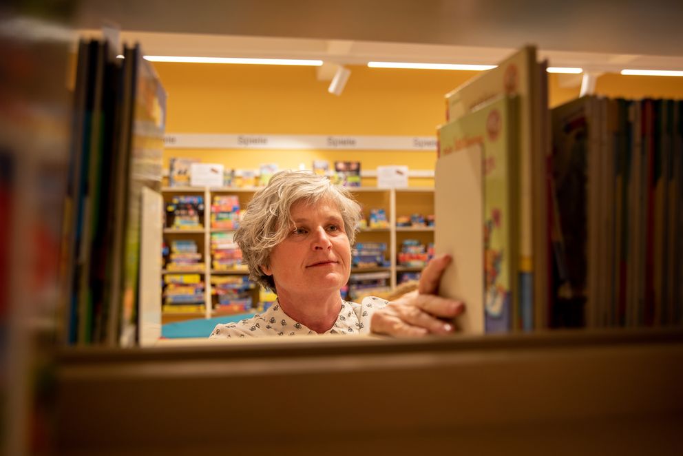 Mitarbeiterin der Gemeindebücherei sortiert Bücher in ein Regal ein